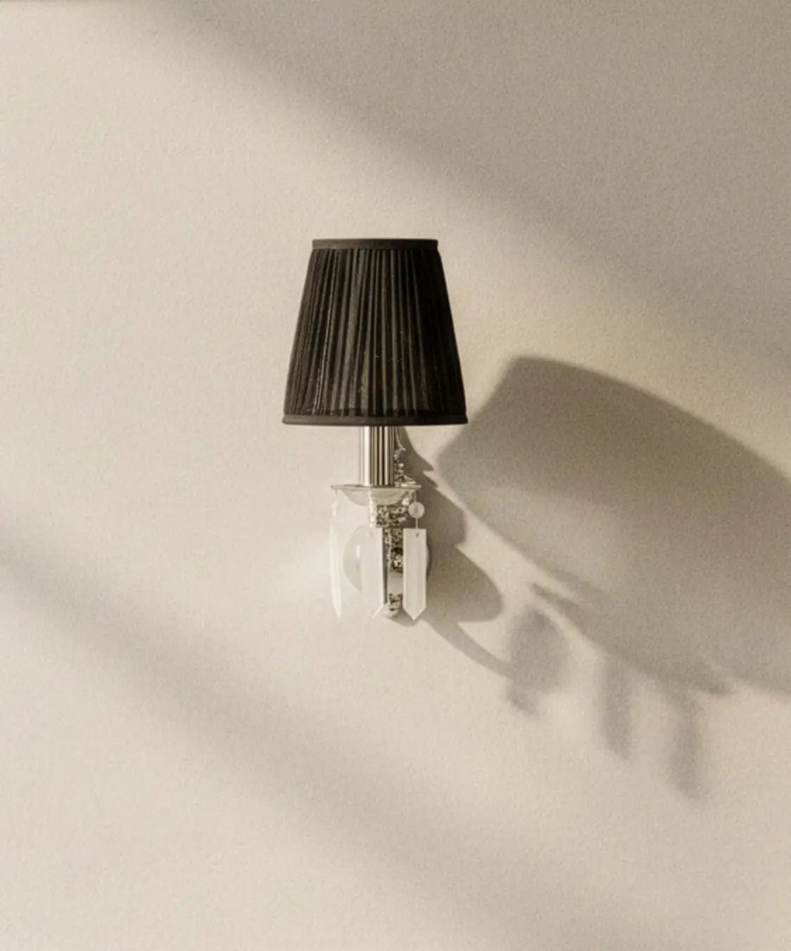 Aplique de pared encendido con pantalla cónica negra plisada y estructura plateada."
