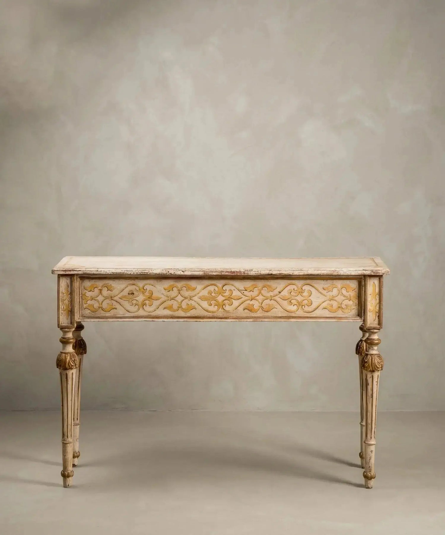 Consola neoclásica de madera pintada en marfil y oro con patas estriadas y motivos florales frontales.