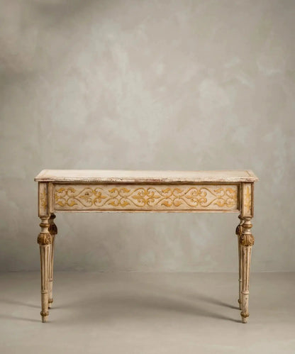 Consola neoclásica de madera pintada en marfil y oro con patas estriadas y motivos florales frontales.