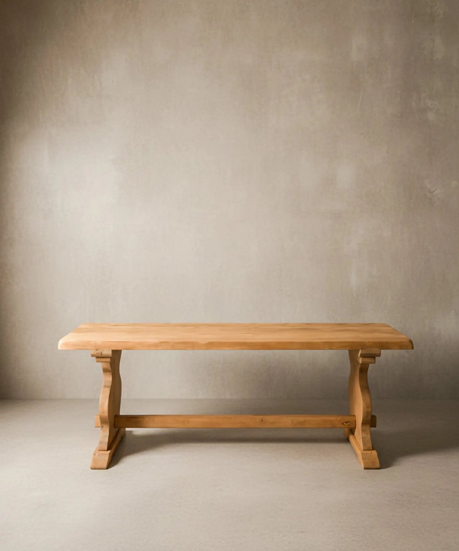 Mesa de comedor rústica de madera maciza vista de frente sobre fondo neutro, destacando el tablero grueso y el travesaño central.