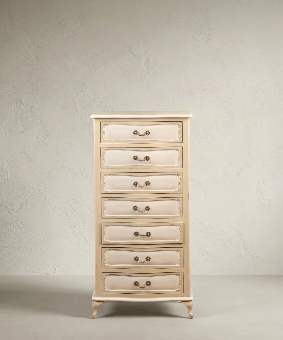 Semanier francés de 7 cajones en color crema y blanco, vista tres cuartos mostrando molduras y patas cabriolé sobre fondo neutro.