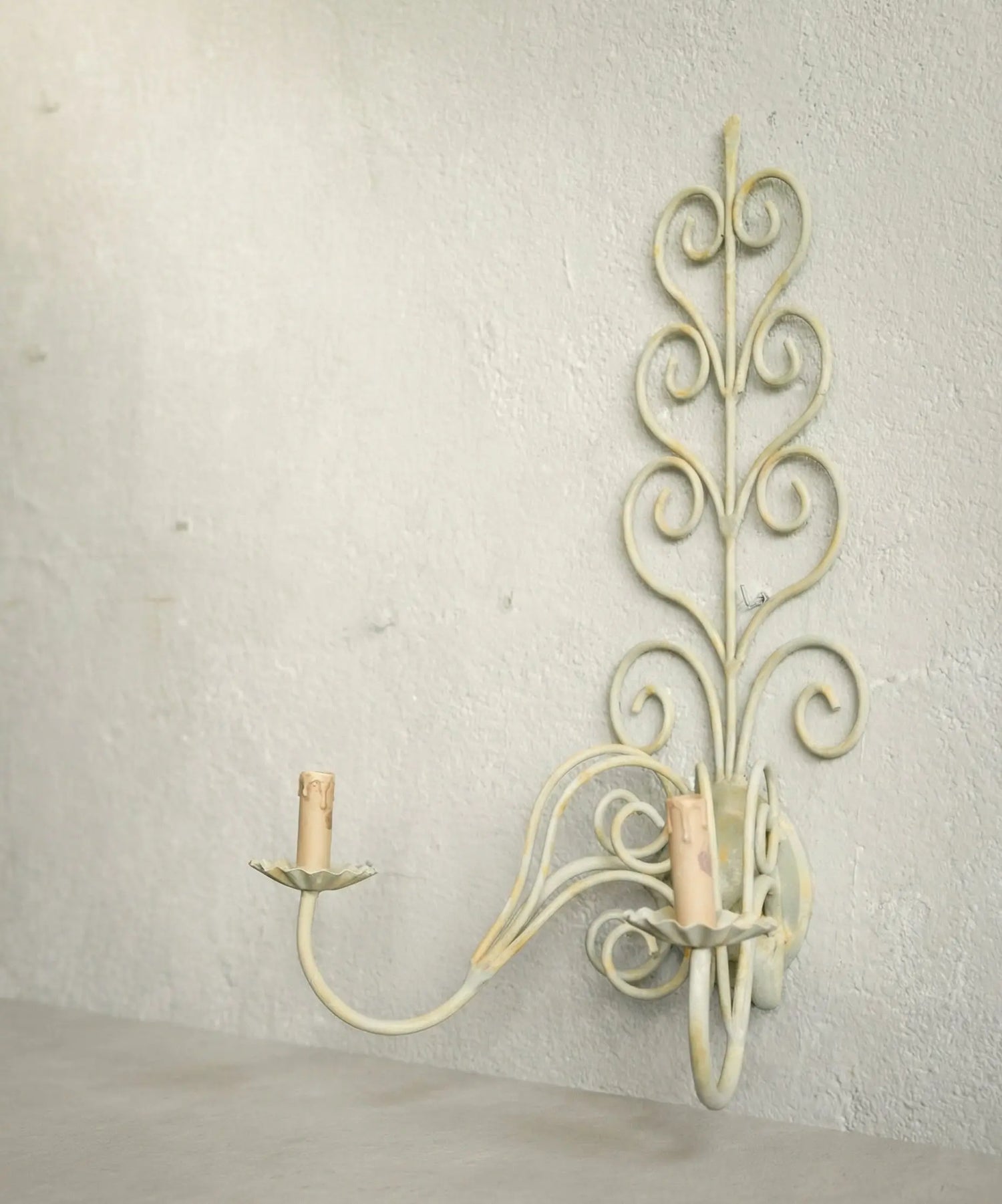 Perfil de aplique de forja antiguo mostrando los brazos curvos y la pátina desgastada.