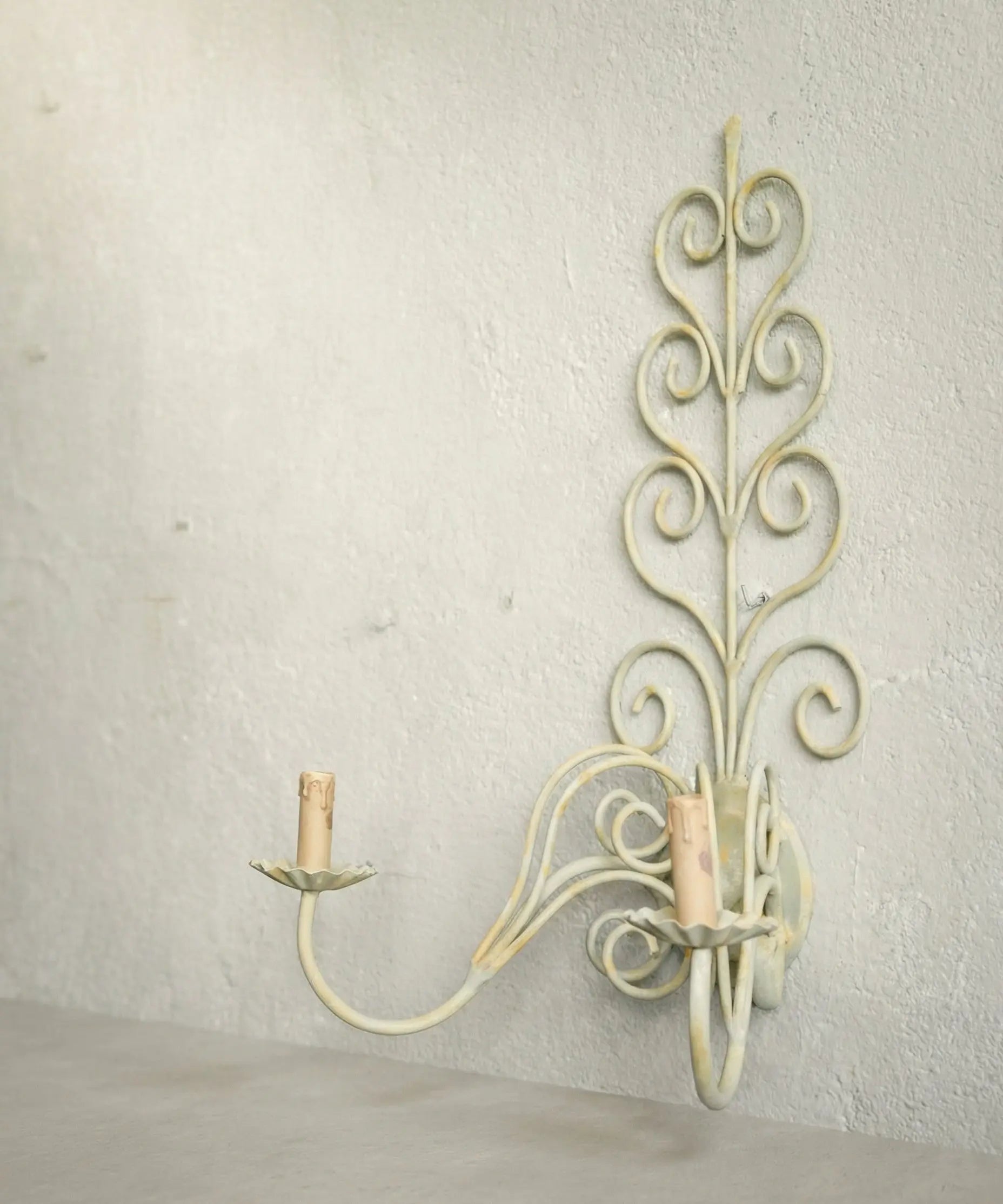 Perfil de aplique de forja antiguo mostrando los brazos curvos y la pátina desgastada.