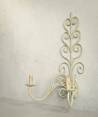 Perfil de aplique de forja antiguo mostrando los brazos curvos y la pátina desgastada.