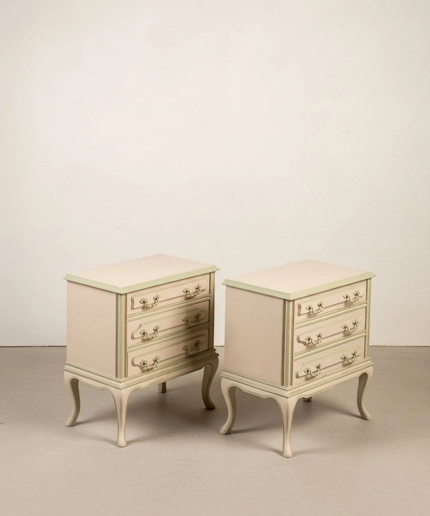 Pareja de mesitas de noche vintage de tres cajones pintadas en beige y verde salvia con patas curvas.