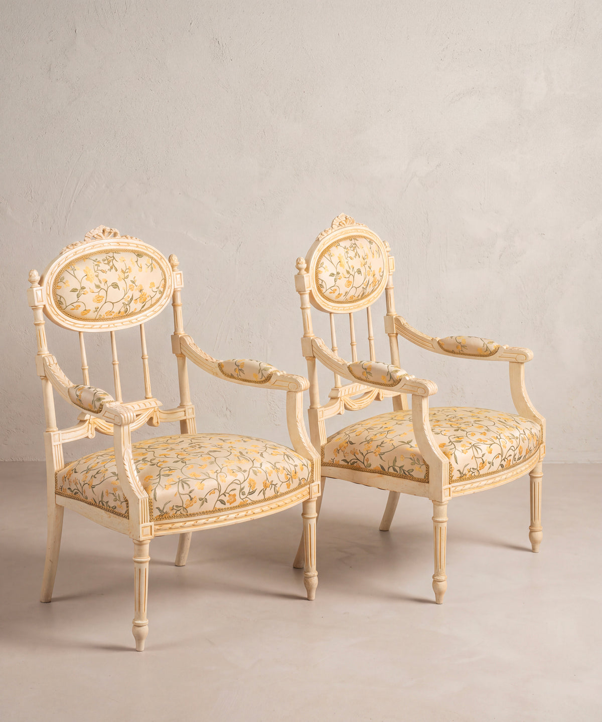 Pareja de sillones pintados en crema vista lateral con brazos tallados y faldón de cinta — Antique Arte y Decoración