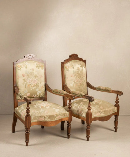 Pareja de sillones antiguos estilo neoclásico con tapicería floral sobre fondo de papel pintado paisajístico sepia.