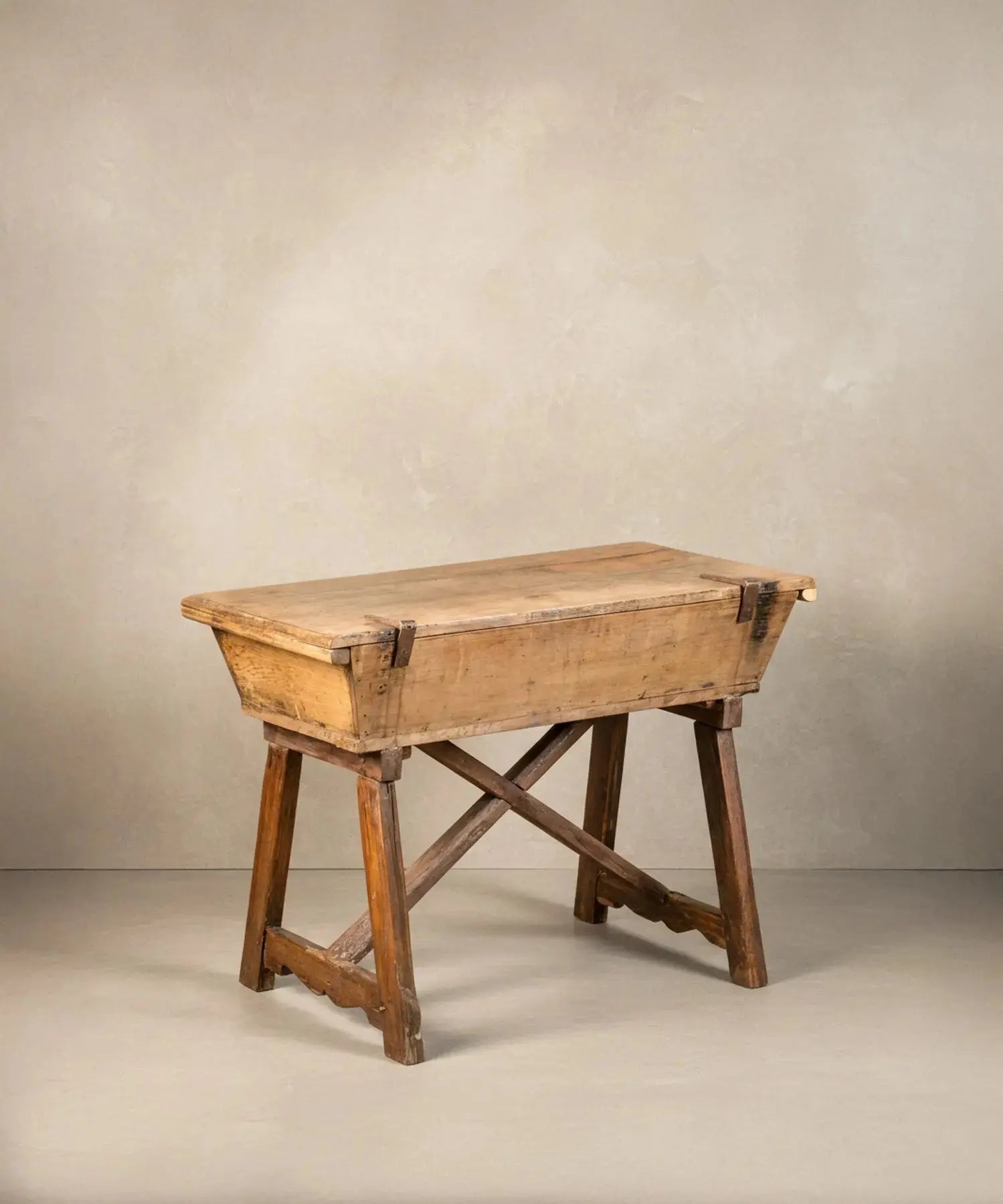 Mesa artesa antigua de madera maciza con tapa cerrada sobre fondo neutro, estilo rústico.