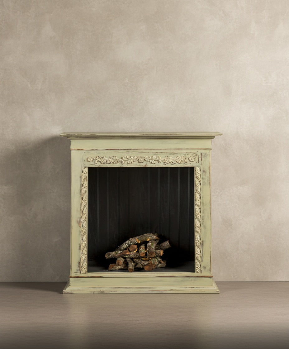  Vista frontal de la chimenea decorativa verde pátina con talla floral sobre fondo neutro.