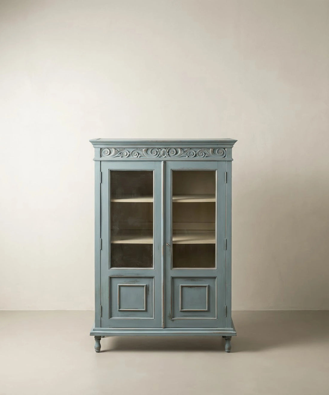 Vitrina estilo provenzal azul empolvado con puertas de cristal y friso tallado.